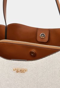 Sac fourre-tout marron et crème avec un extérieur perforé, poche zippée et détail logo doré. Dispose d'un fond plat et de deux poignées.