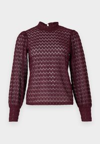 Bordeaux højhalset top lavet af tekstureret strik, med lange pufærmer og et bølget mønster. Lynlås bagpå.