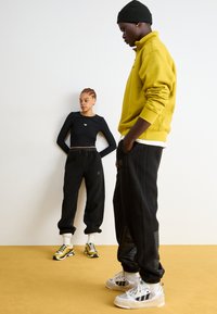 Čierny skrátený top s dlhými rukávmi, čierne flísové jogger nohavice a žltý pulóver. Tenisky majú kovové zlaté detaily. Textúrované čierne nohavice.