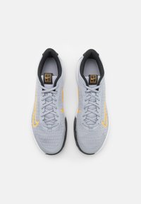 Un paio di scarpe da ginnastica grigio chiaro con logo arancione a forma di baffo, rivestimento interno nero e lacci, mostrato dall'alto su uno sfondo bianco.