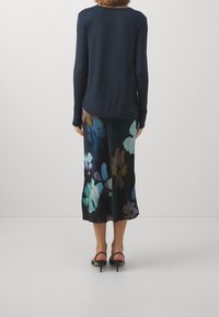 Navy pitkät hihat -paita yhdistettynä valuvaan mustaan hameeseen, jossa on värikäs kukkakuosi sinisen, purppuran ja vihreän sävyissä. Mustat korkokengät.