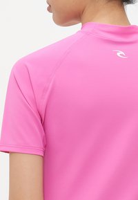 Close-up of person wearing bright pink short-sleeve athletic shirt with a small white logo on the upper back.