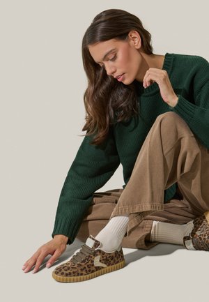 Baskets imprimées léopard avec suède texturé, semelle en caoutchouc beige et lacets marron, associées à un pull vert et un pantalon en velours côtelé beige.
