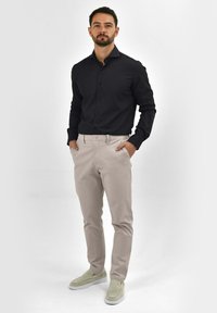 Zwarte button-up shirt, lichtbeige broek en instap schoenen. Het shirt heeft een gladde textuur en een klassieke kraag; de broek is goed gesneden.