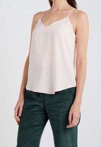 Top sans manches rose clair avec un décolleté en V ; tissu lisse, coupe décontractée et fines bretelles spaghetti, associé à un pantalon en velours côtelé vert texturé.