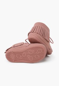 Botas mocasines de ante rosa con acentos de flecos, punta redondeada y suelas de goma texturizadas con un patrón ondulado. Cordones asegurados en la parte posterior.