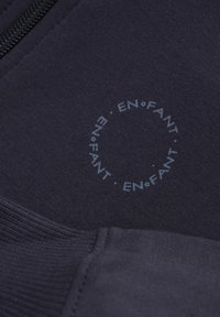 Tma navy látka s potiskem kruhového loga "EN•FANT". Hladká textura s detaily na zipovém zavírání.