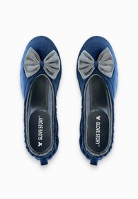 Ballerines bleu marine en matériau doux, avec un nœud en tissu gris sur le devant, des côtés élastiques et une semelle extérieure lisse et transparente.