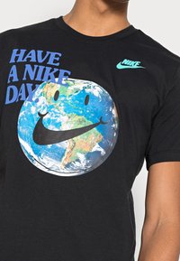 Svart bomulls t-shirt med en globdesign med ett smiley-ansikte, Nike-logotyp i aqua och blå text som säger "HAVE A NIKE DAY."