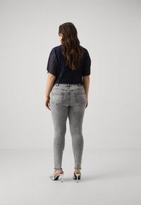 Navy pleated top with short sleeves paired with gray skinny jeans and silver heels, featuring a distressed hem and back pockets.