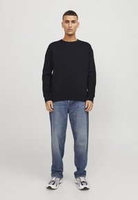 Sudadera azul marino oscura con cuello redondo, puños y dobladillo acanalados, combinada con jeans azul claro y zapatillas deportivas gris-negro.