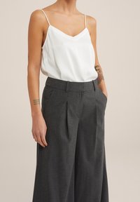 White satin cami top with thin straps, paired with high-waisted charcoal gray tailored trousers featuring pleats and side pockets.