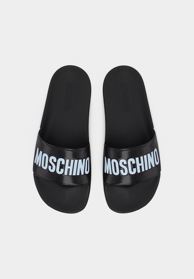 Μαύρα σανδάλια τύπου slip-on με φαρδιές λουριά που φέρουν λευκή επιγραφή "MOSCHINO" στο πάνω μέρος, τοποθετημένα δίπλα δίπλα σε απλό φόντο.
