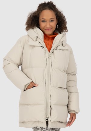 Veste bouffante légère beige clair avec un col haut, une fermeture éclair et des poches latérales. Elle présente une texture douce et une coupe décontractée.