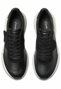 Zapatillas de cuero negro y ante con cordones planos, lengüeta acolchada y suelas de goma blanca. Diseño sencillo y detalles de textura contrastante.