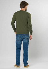 Camisa de manga larga verde oliva con cuello redondo, combinada con jeans azules que tienen dos bolsillos traseros y una textura de denim claro.