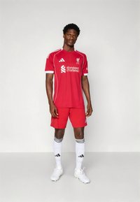Röd Liverpool FC-tröja och shorts med vita detaljer och logotyp. Bärs med vita strumpor och fotbollsskor, vilket visar en atletisk design och passform.