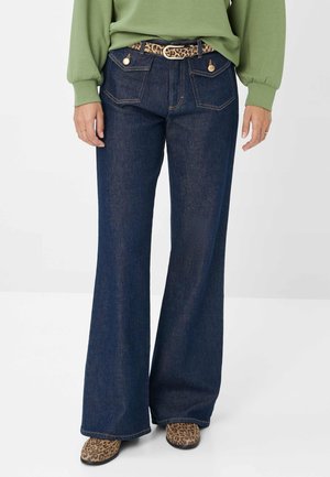Donkere denim wijde broek met gouden accenten, voorzien van achterzakken en een luipaardprint riem. Gedragen met beige luipaardprint schoenen.
