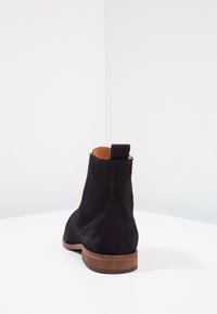 Stivale alla caviglia in suede nero con punta tonda, tacco basso in legno e linguetta sul retro; presenta cuciture a contrasto lungo le cuciture.