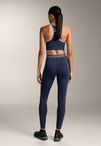 Tengerészkék sportmelltartó és leggings szett kontrasztos színű csíkokkal, testhez simuló kialakítással, rugalmas anyagból és sima textúrával.