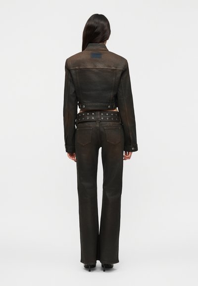 Γυναίκα που στέκεται γυρισμένη από πίσω, φοράει εφαρμοστή cropped σκούρα καφέ ζακέτα, ταιριαστό παντελόνι με φαρδιά ποδών και φαρδιά ζώνη με μεταλλικά τρύπες.