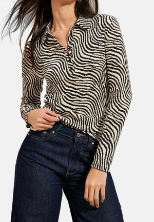 Femme portant un haut à manches longues rayé zèbre avec des boutons et un jean taille haute bleu foncé, posant avec la main près de la taille.