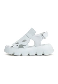 White leather sandal with cut-out details, a closed toe, and thick white sole featuring a wave pattern and adjustable ankle strap.