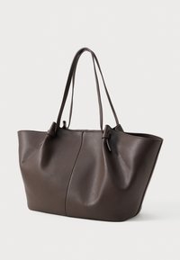 Borsa tote in pelle marrone scuro con due lunghe tracolle e una cucitura sottile al centro, posizionata su uno sfondo chiaro e neutro.