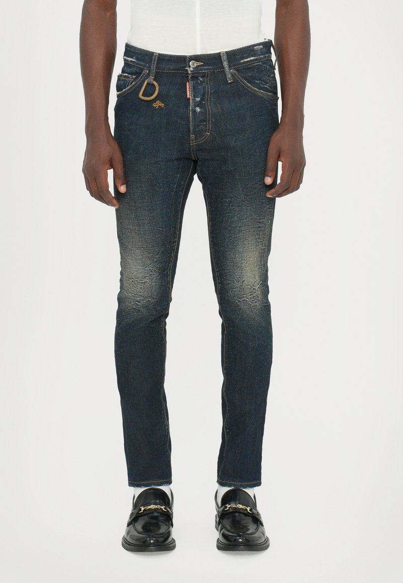 Dark blue denim jeans with a slim fit, light fading, and a subtle distressed texture. Features gold-tone hardware and a D-shaped accent.