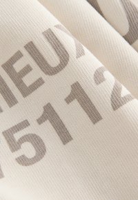 Baumwollstoff mit einer strukturierten Oberfläche, in einer cremefarbenen Ausführung, versehen mit großen grauen Zahlen und Buchstaben, die in einer kräftigen, modernen Schrift gedruckt sind.