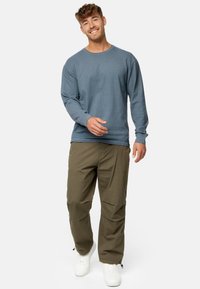 Blaues langärmliges Crewneck-Oberteil aus strukturiertem Stoff, kombiniert mit olivgrünen Cargo-Hosen mit seitlichen Taschen und weißen Sneakers.