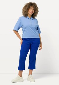 Polo shirt azzurro chiaro con maniche corte e dettaglio dei bottoni, abbinato a pantaloni cropped blu e sneakers bianche con suola spessa.