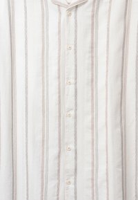 Chemise boutonnée avec des rayures verticales en blanc, beige et gris. Tissu texturé avec un col et cinq boutons sur le devant.