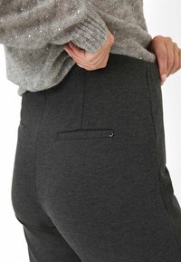 Graue Hose mit weicher Textur, ausgestattet mit einer Gesäßtasche mit schmalem Rand und kleinen hardware Details. Getragen mit einem glitzernden grauen Pullover.