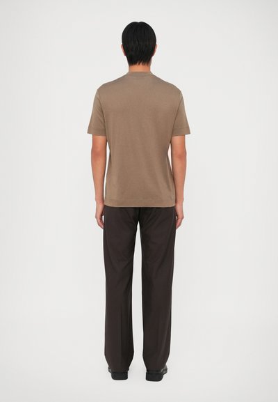 Camiseta de algodón marrón con mangas cortas, cuello redondo y costuras laterales, combinada con pantalones negros de corte holgado, vista desde la espalda.