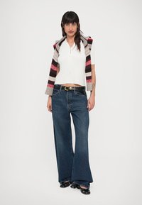 White, short-sleeve top with a scoop neck layered under a multicolored striped knitted vest. Wide-leg blue denim jeans, black shoes.