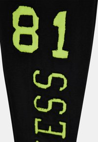 Tissu noir avec une finition texturée arborant des chiffres néon verts audacieux "81" et "SS" dans une police de caractère stylisée.