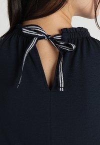Top navy con un agujero en la espalda asegurado con un lazo, acentuado por detalles a rayas y una tela texturizada.