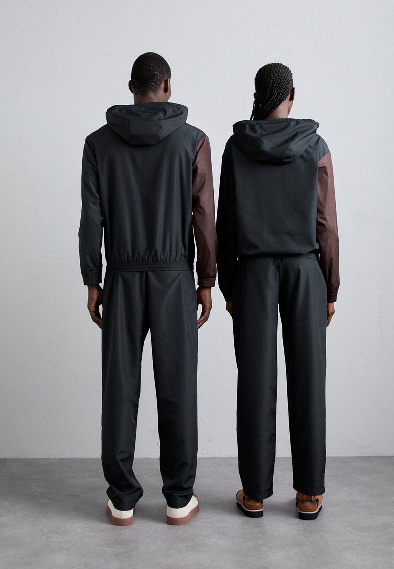 Des vestes à capuche noires et brunes avec des poignets élastiques, assorties à des pantalons noirs. Les vestes présentent des couleurs de manches contrastantes et une coupe décontractée.