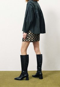 Camicia nera a maniche lunghe con schiena plissettata, abbinata a una minigonna leopardata. Il modello indossa stivali neri in pelle al ginocchio con tacco a blocco.