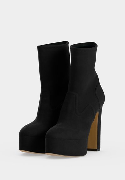 Paire de bottines noires à plateforme avec talons carrés hauts et bouts ronds sur un fond uni.