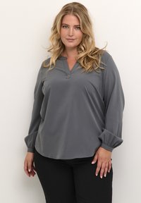 Gray long-sleeve blouse with a V-neckline, soft fabric, gathered cuffs, and a relaxed fit, paired with black pants.