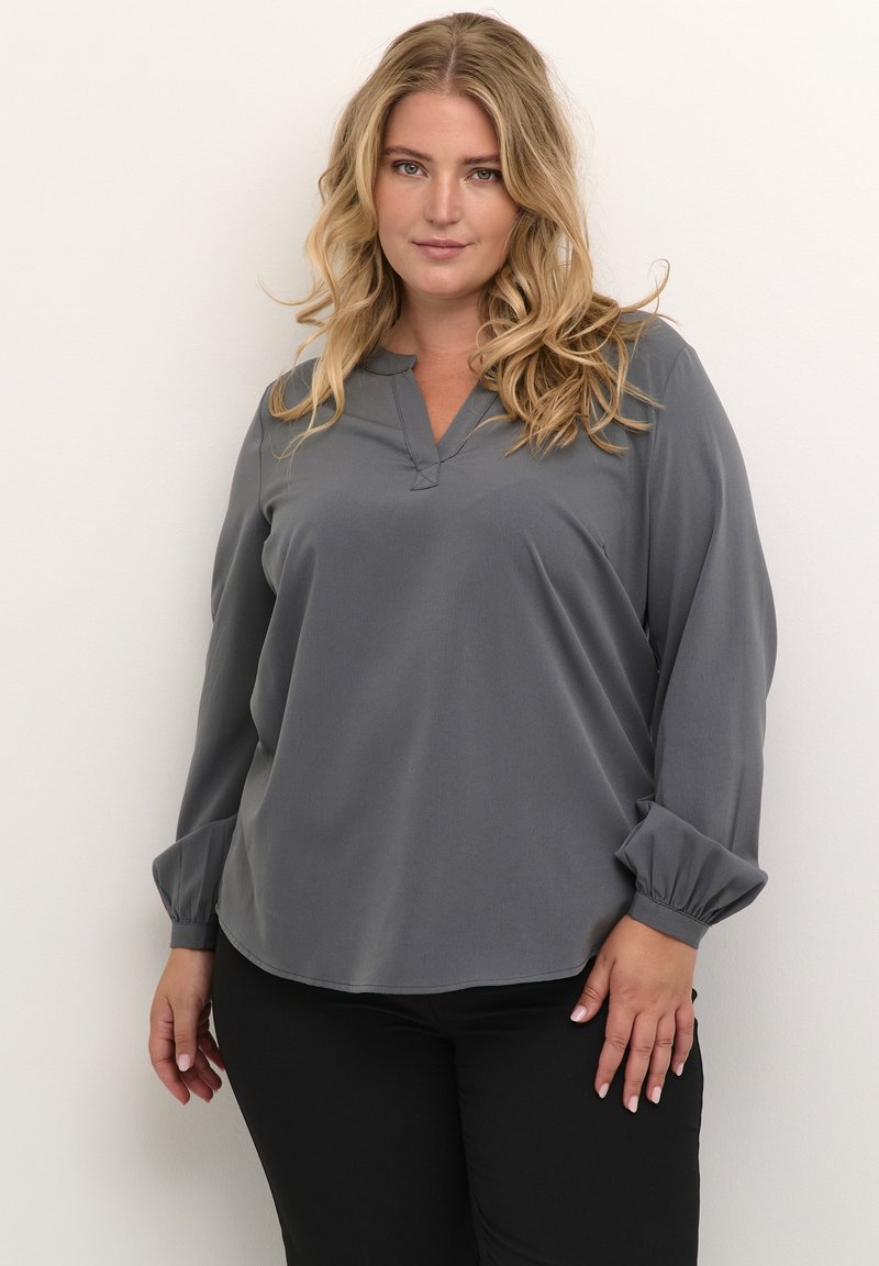 Gray long-sleeve blouse with a V-neckline, soft fabric, gathered cuffs, and a relaxed fit, paired with black pants.