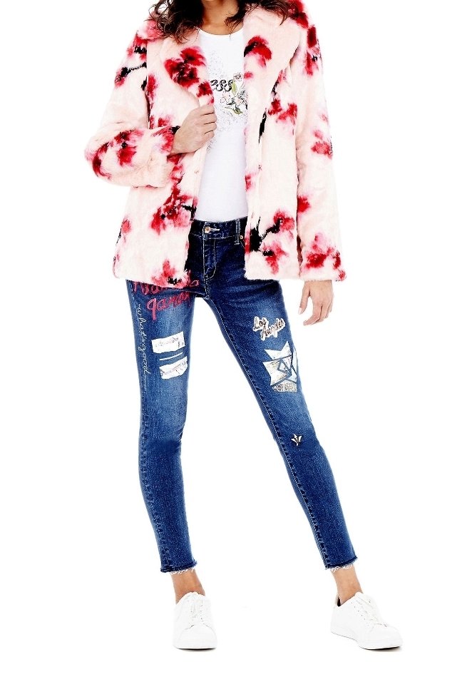 Femme portant une veste en fausse fourrure à fleurs rose et rouge, un t-shirt blanc à motif graphique, un jean skinny orné de patchs, et des baskets blanches.