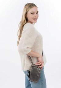 Lichtbeige, fuzzy gebreid sweater met driekwartmouwen; model houdt een kleine, zilverkleurige, gestructureerde crossbody-tas met ritssluiting vast.