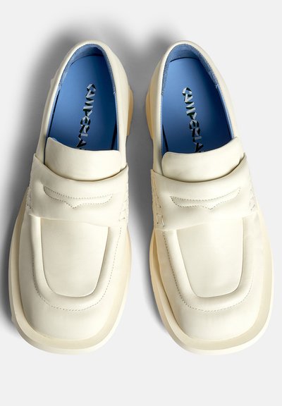 White leather loafers with a rounded toe, stitched detailing, and thick rubber soles; blue insoles with contrasting branding.