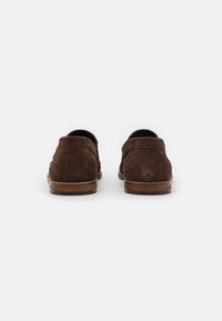 Scarpe in suede marrone con design slip-on, retro arrotondato e suola marrone a contrasto. Presentano cuciture lungo i bordi per un tocco di dettaglio.