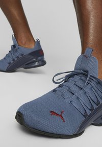 Zapatilla deportiva de color azul claro hecha de malla transpirable, con un panel de acento en azul oscuro, logo rojo y una suela acolchada con superficie texturizada.