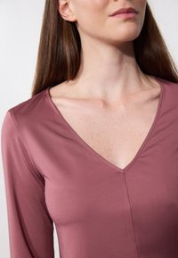 Top de manga larga en color malva con escote en V, textura suave y detalles de costura sutiles, que presenta un diseño ajustado y un estilo minimalista.