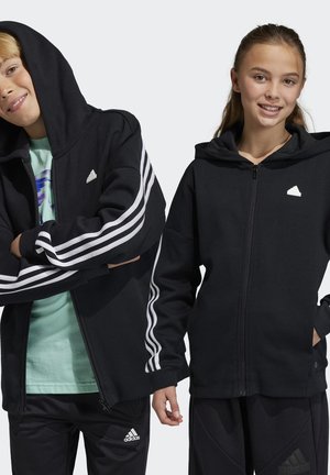 Schwarze Kapuzenjacke mit Reißverschluss aus weichem Stoff, mit weißen drei Streifen als Branding auf den Ärmeln und einem kleinen Logo auf der Brust. Mit angenähter Kapuze.